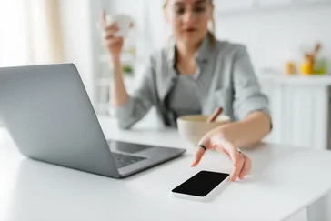 Vrouw grijpt naar smartphone achter bureau